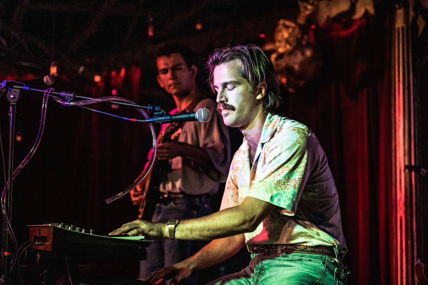 Musician performing on keyboard at a dimly lit concert venue.