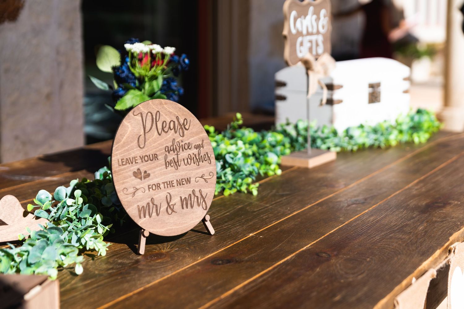 Wooden decor sign with greenery displayed on rustic table at wedding reception.