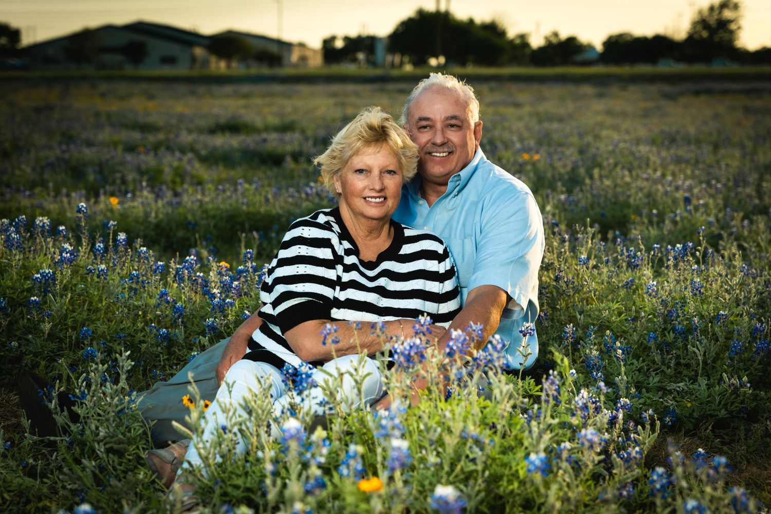 Senior couple sitting together in field of blue wildflowers at sunset.