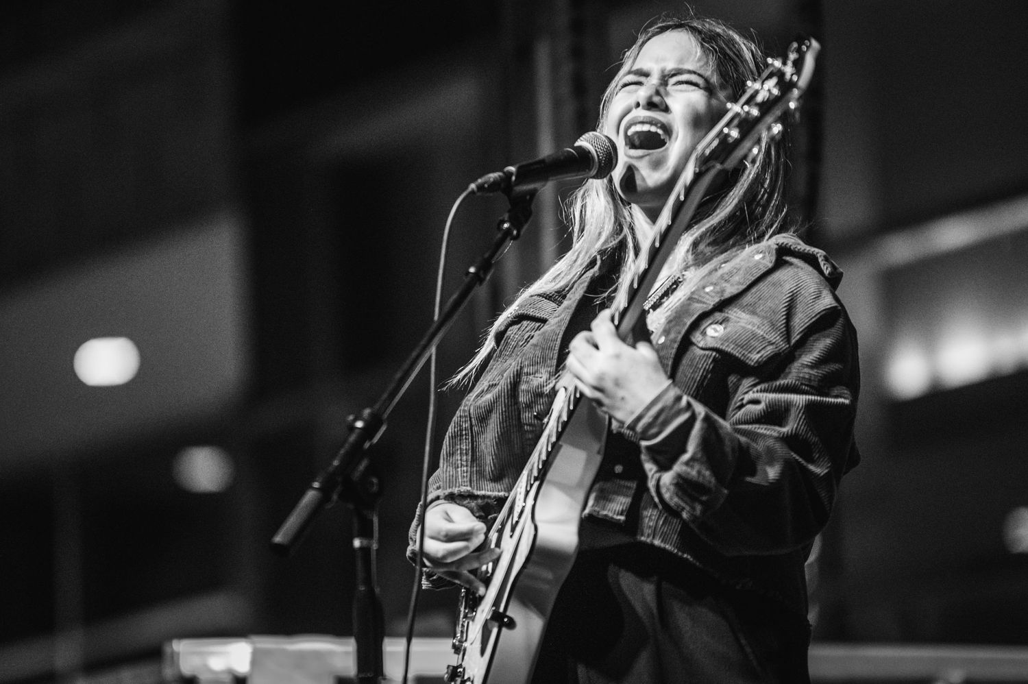 A passionate musician plays acoustic guitar and sings into microphone during a black and white performance shot.