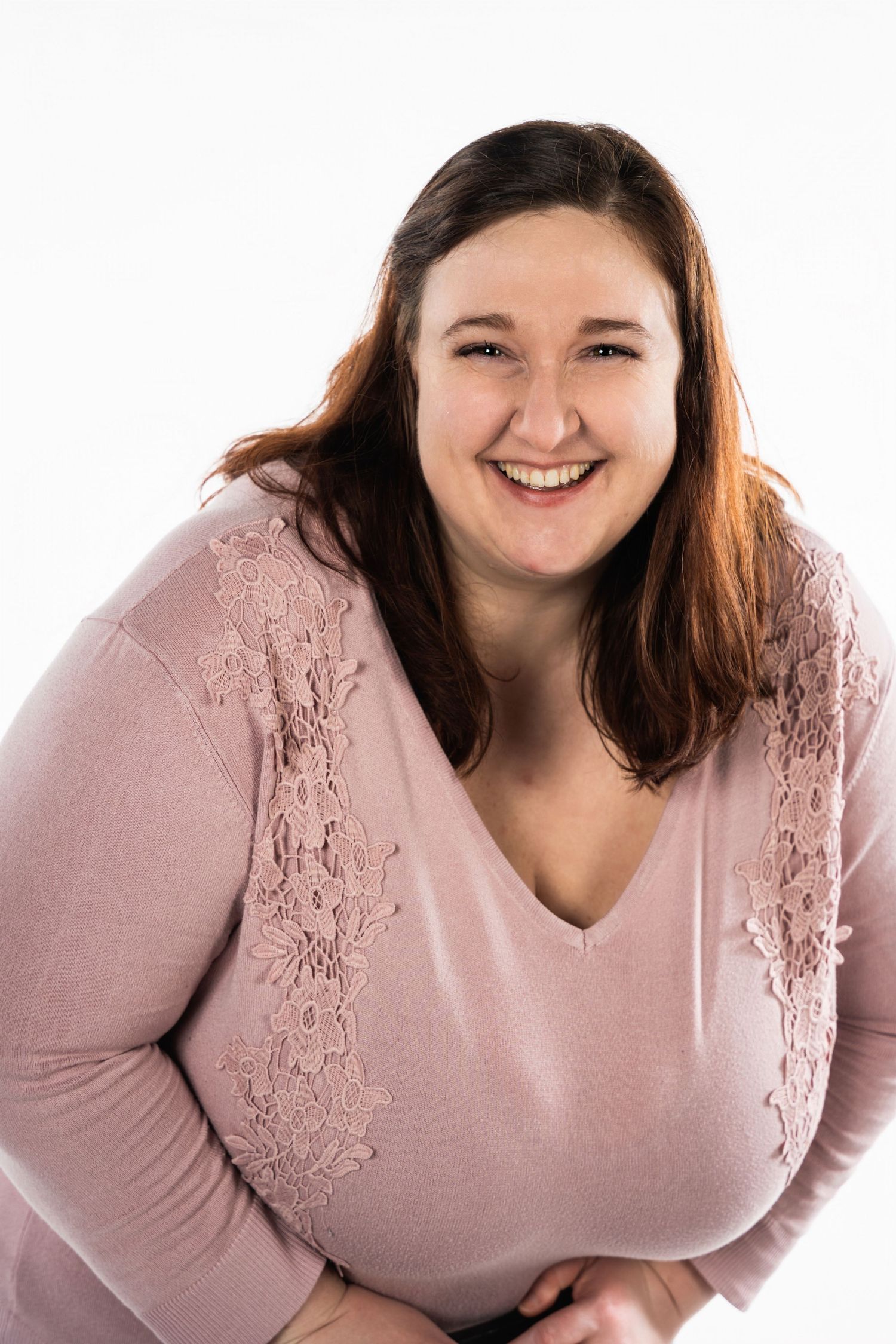 A person wearing a pink lace sweater poses for a studio portrait with a warm smile.