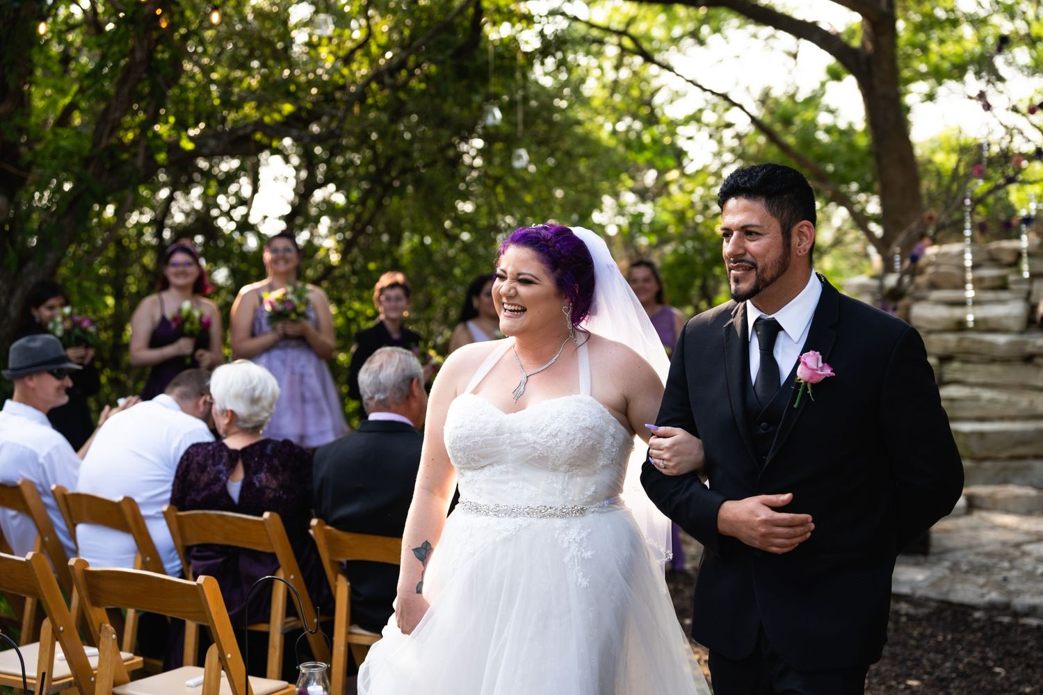 Wedding couple walks down the aisle after ceremony with guests seated in wooden chairs outdoors.