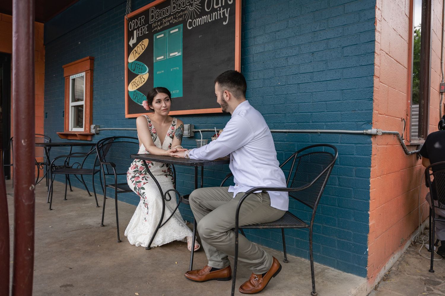 A couple shares an intimate cafe moment at an outdoor table against a blue painted brick wall.
