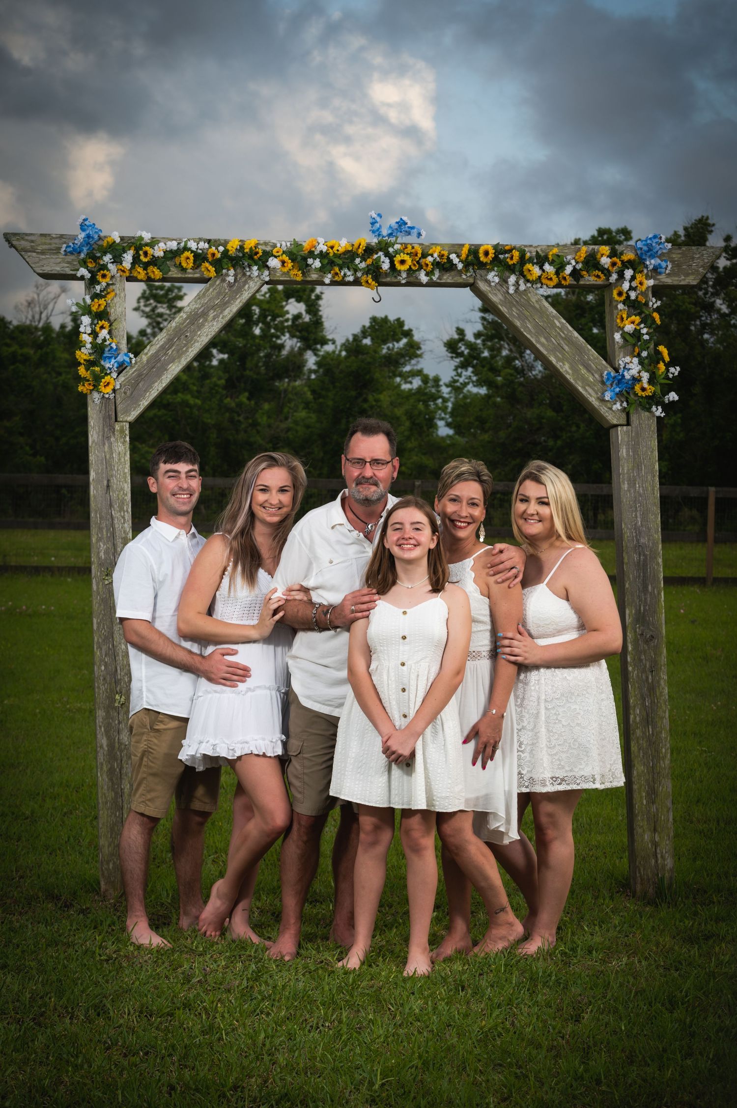 Family group photo under a flower-decorated arch in coordinated white and khaki outfits.