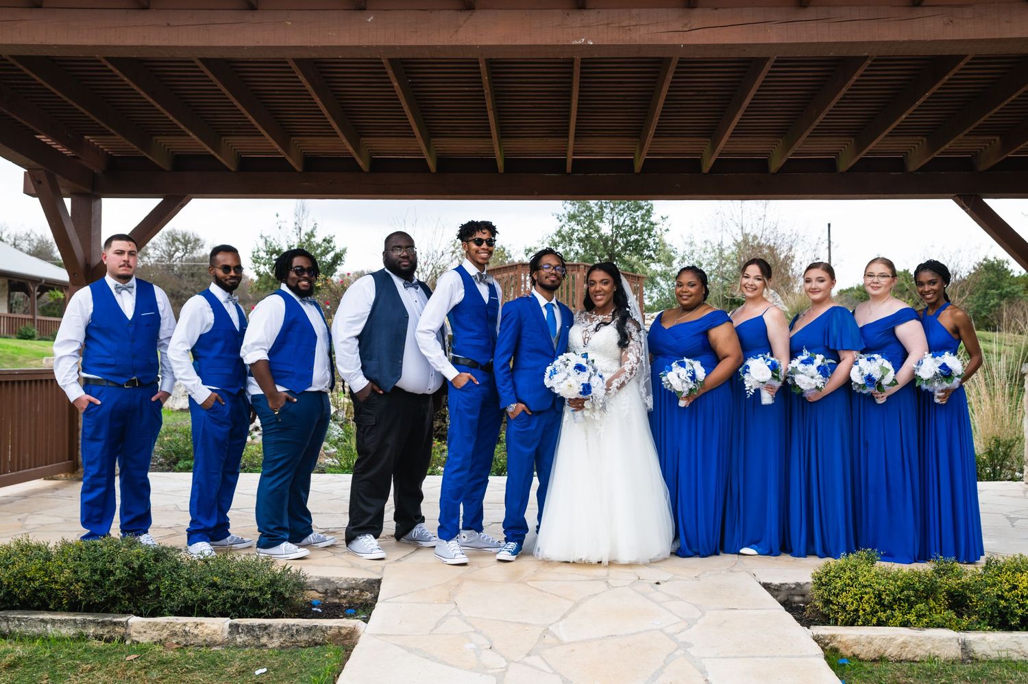 Wedding party lines up outdoors wearing coordinated royal blue and white formal attire.