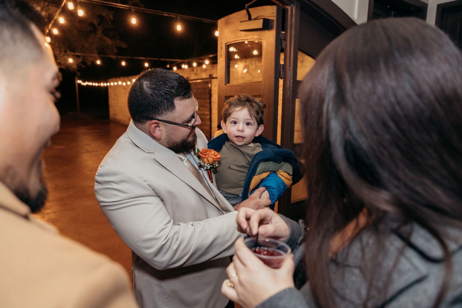 Adults gather around small child at indoor evening celebration.