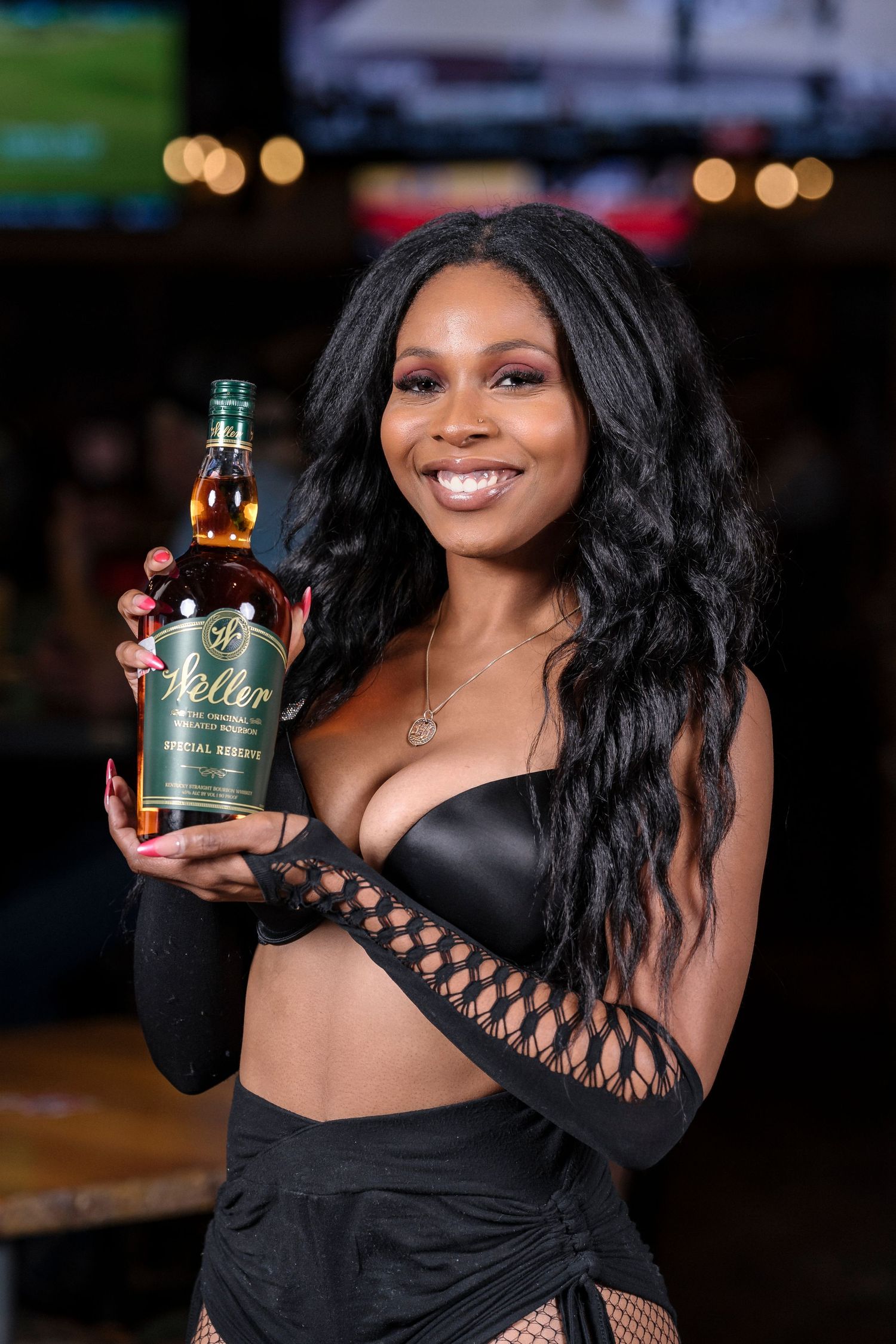 Model displays green bottle of spirits while posing in bar setting.