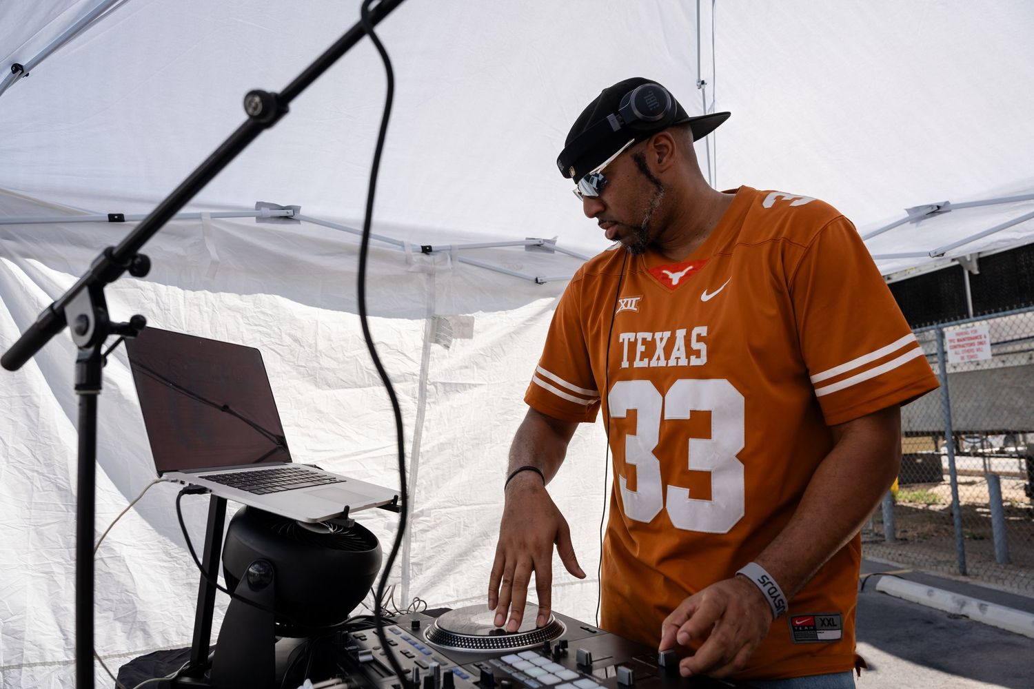 DJ in orange Texas jersey performs at outdoor event under white tent.