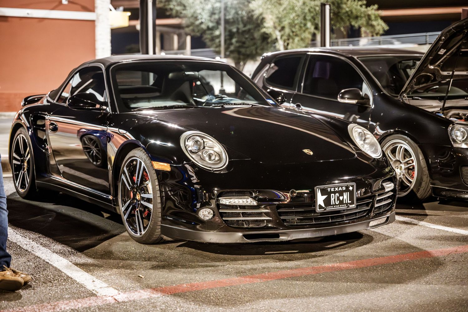 A black Porsche 911 with custom wheels parked at a nighttime car meet.