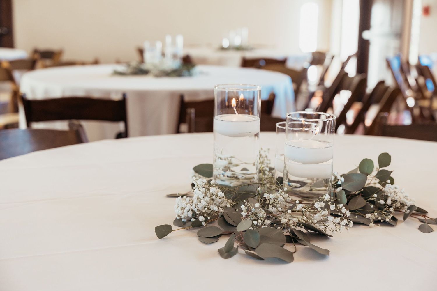Minimalist table decor with greenery and glass candle holders at wedding reception.