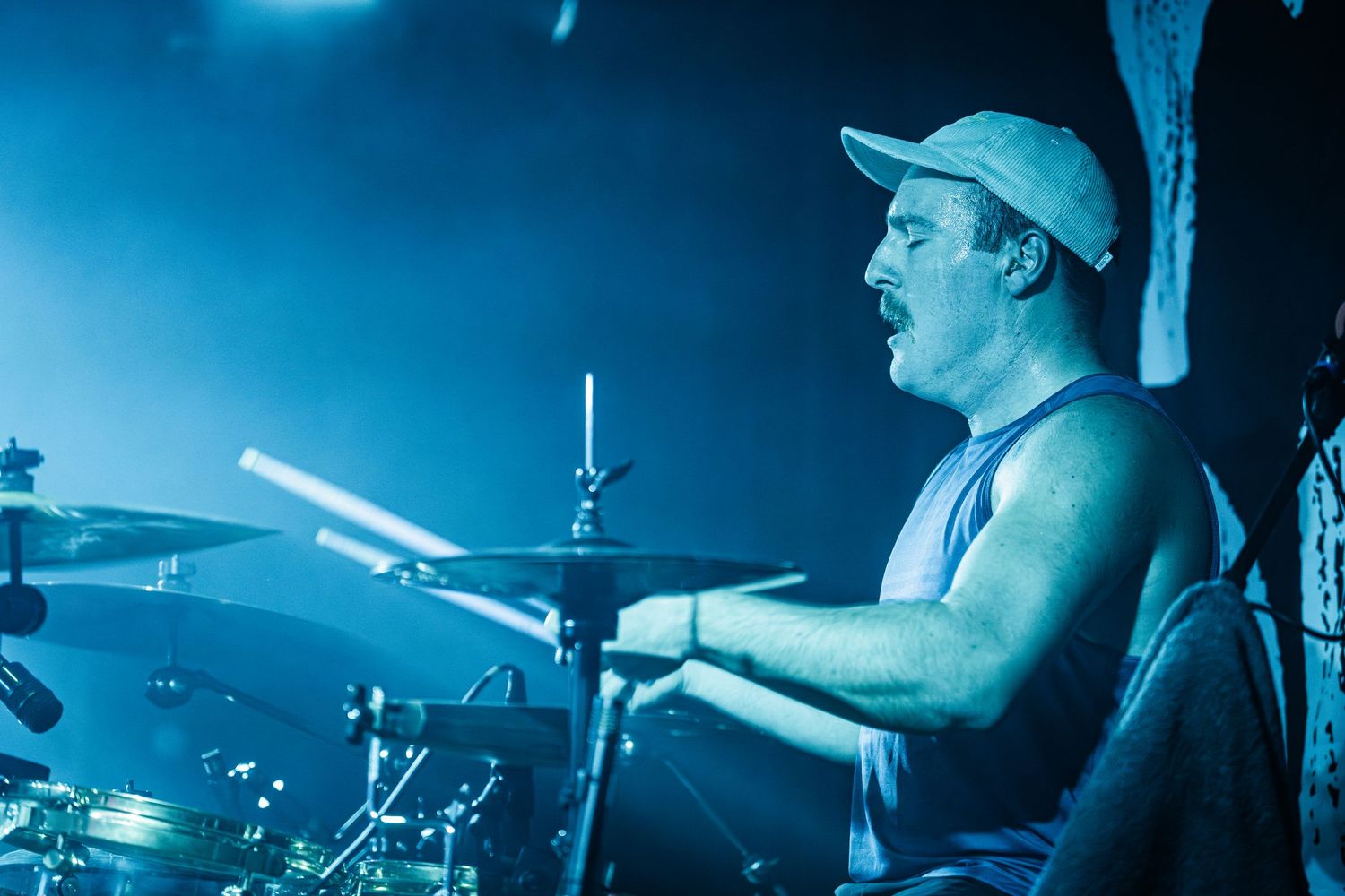 Drummer performing on stage bathed in blue concert lighting.