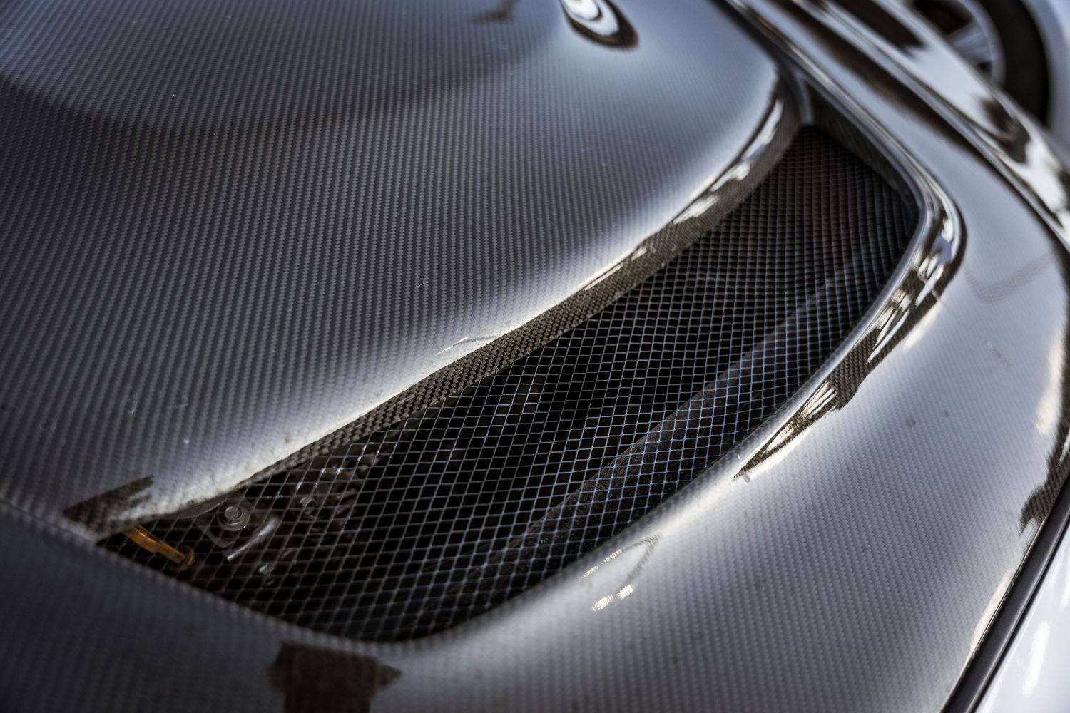 Detail shot of black carbon fiber hood vent on performance car.