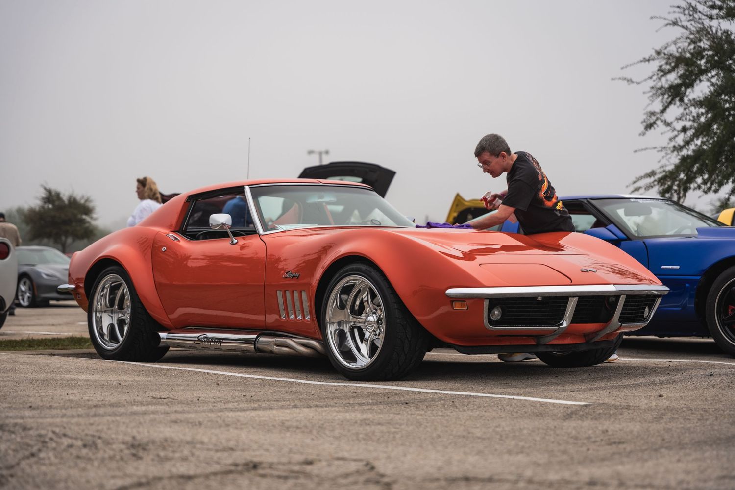 A classic orange Chevrolet Corvette Stingray with custom wheels at a car show.