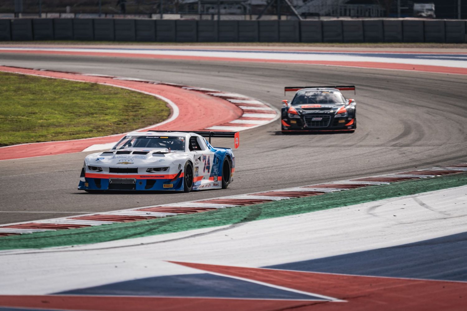 Two race-spec Porsches competing on a professional racing track with red and white curbing.