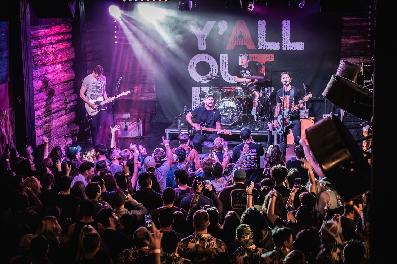 Energetic concert crowd at a rock show with 'Y'all Out' signage and stage lighting.