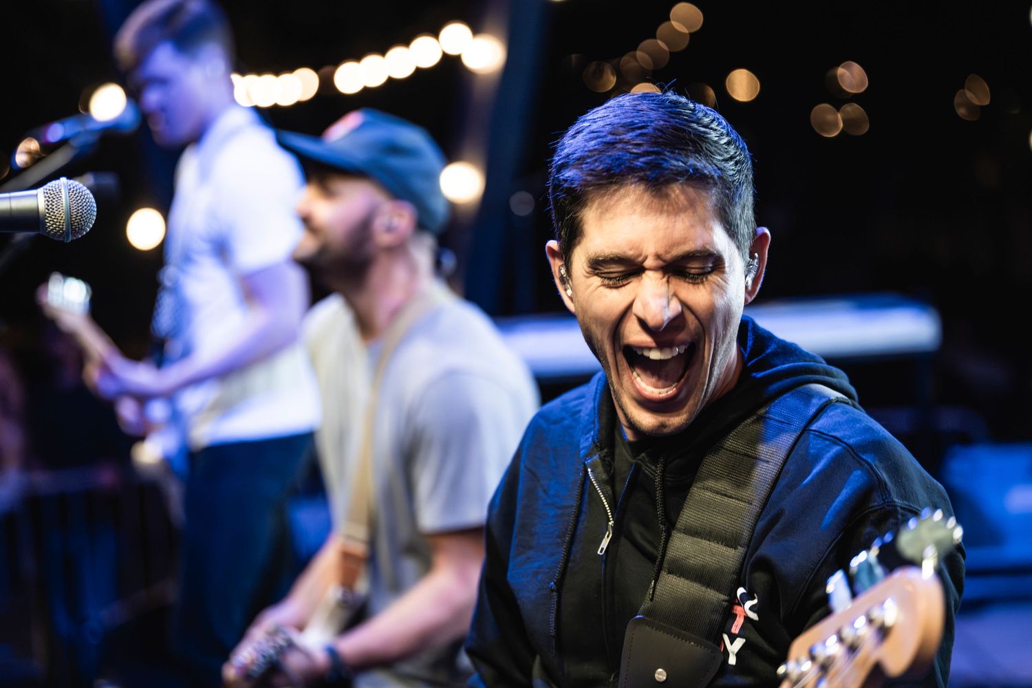 Musicians performing passionately on stage with guitars under concert lighting.