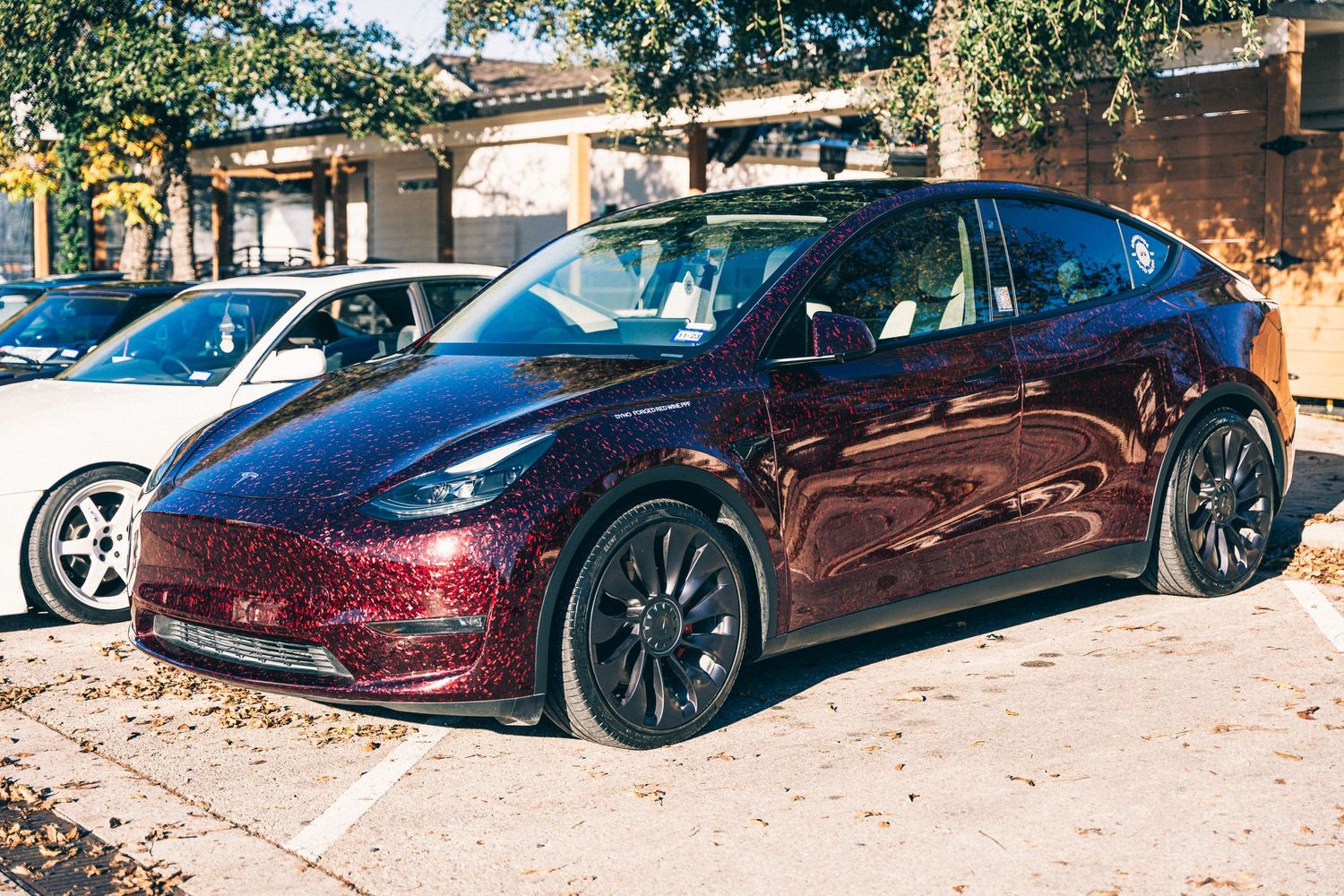 Metallic burgundy Tesla Model Y parked in an outdoor car show.