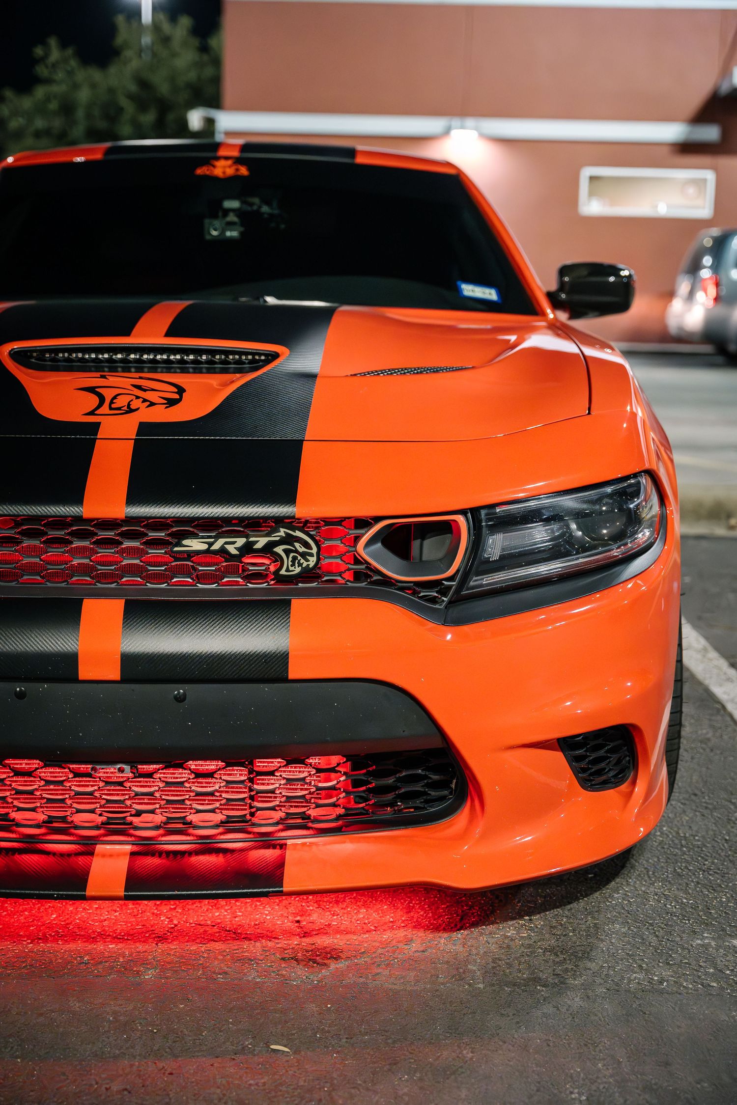 Close-up of an orange Dodge Charger Hellcat's front end showing aggressive styling and racing stripes.