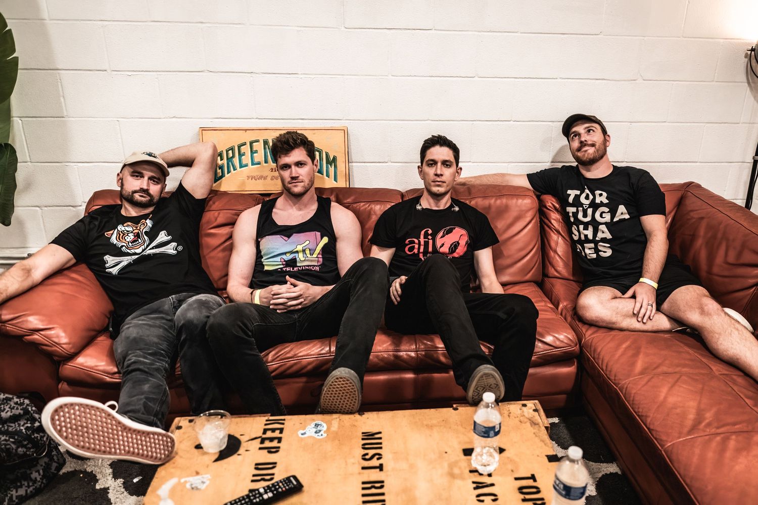 Band members lounge on a sectional brown leather couch with guitars on the floor.
