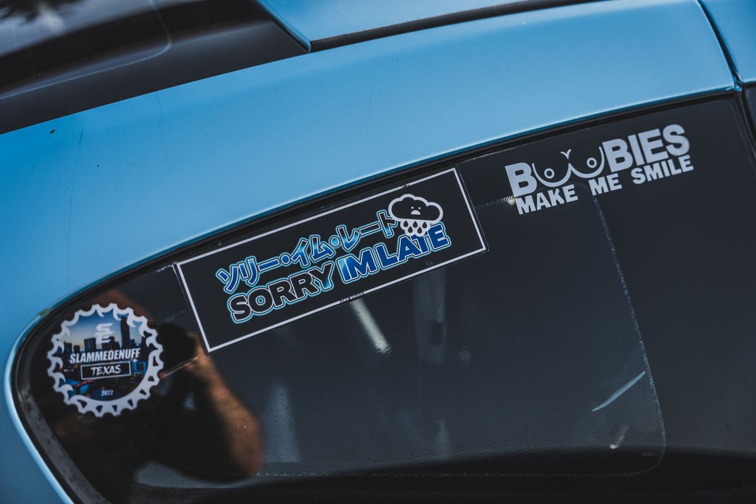 Car window stickers showing Boobies Make Me Smile text decal on blue paint.