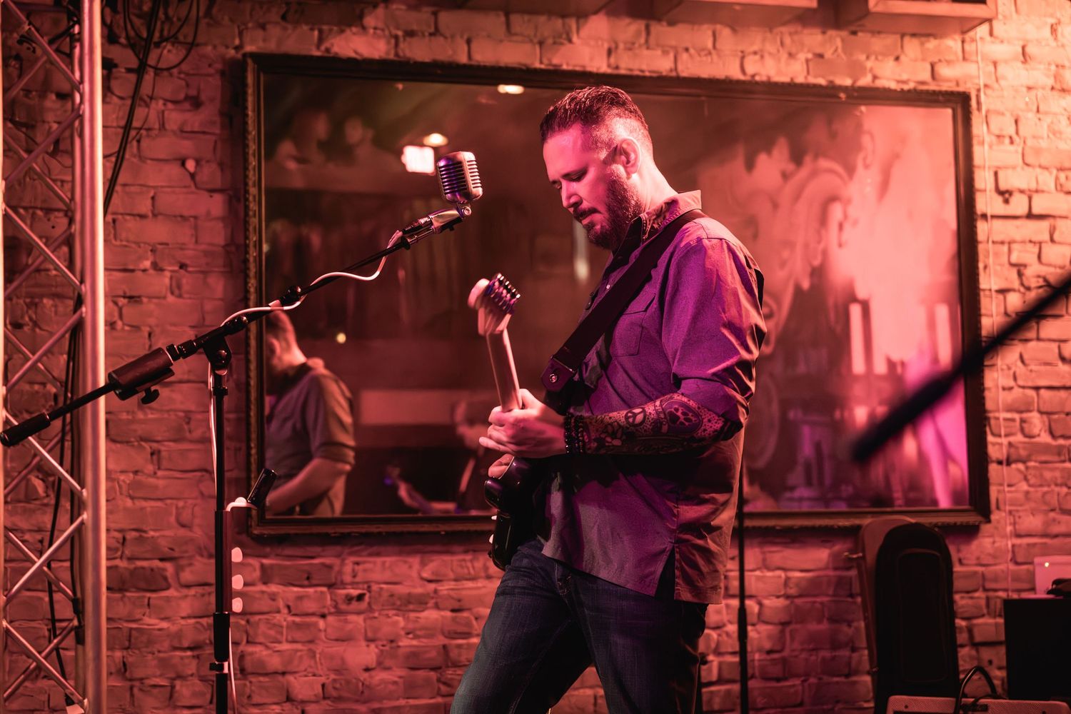 Guitarist performs in front of brick wall under red stage lighting.