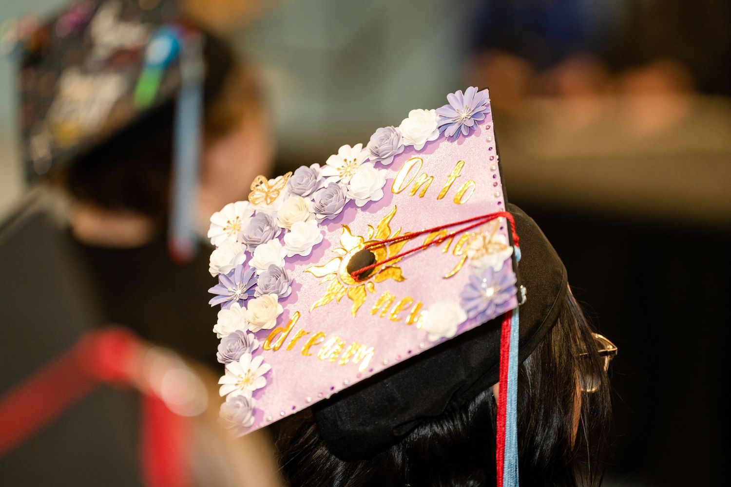 Decorated graduation cap adorned with purple flowers visible during commencement ceremony.