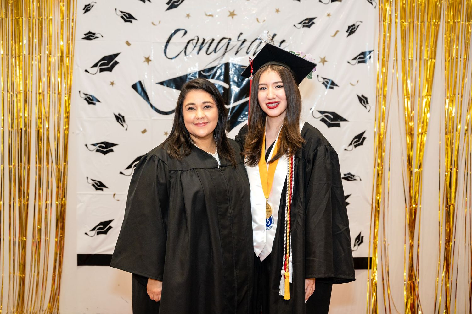 Graduation celebration with decorative gold backdrop and floating mortarboard pattern.