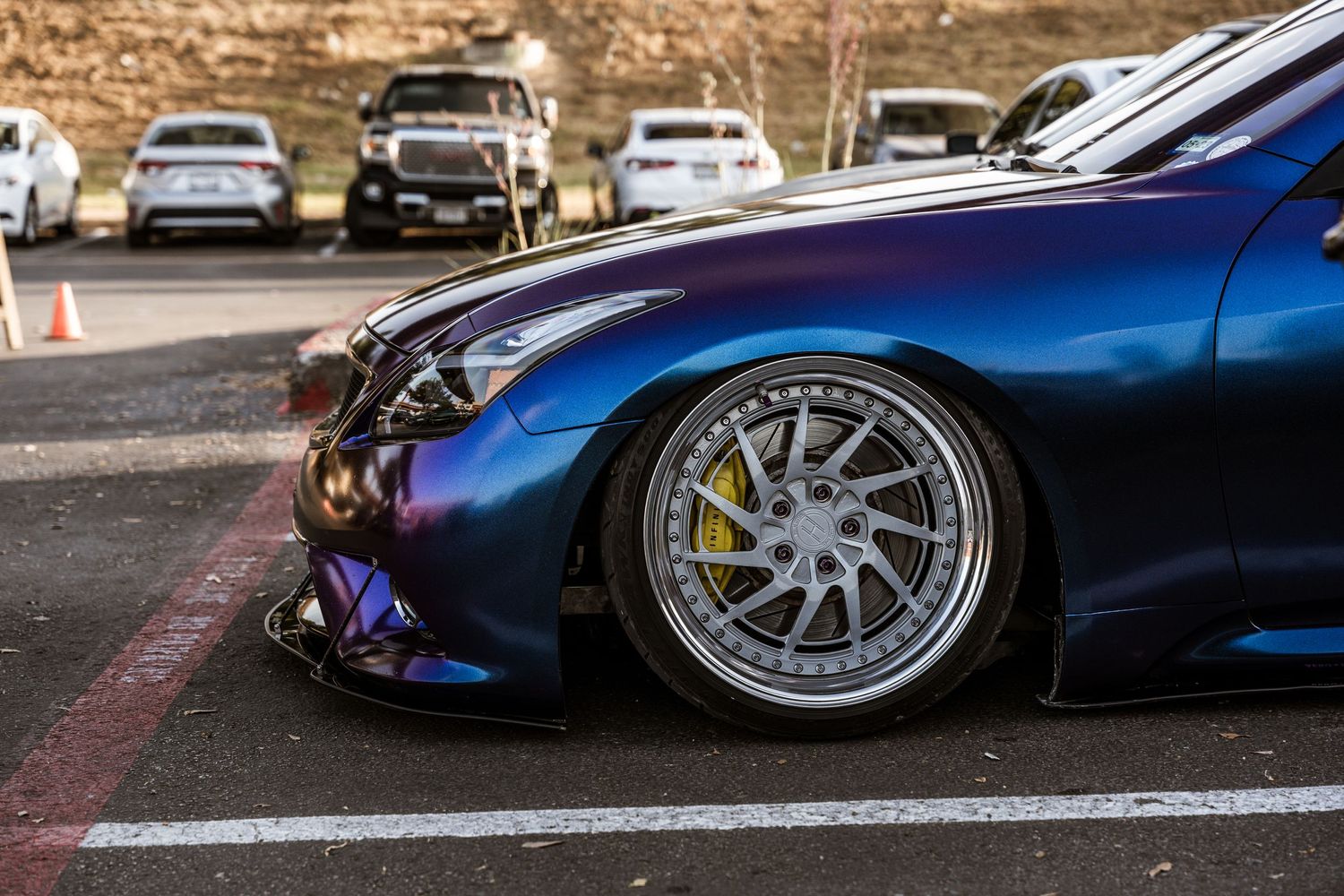 A modified blue sports car with custom wheels and yellow brake calipers in a parking lot.