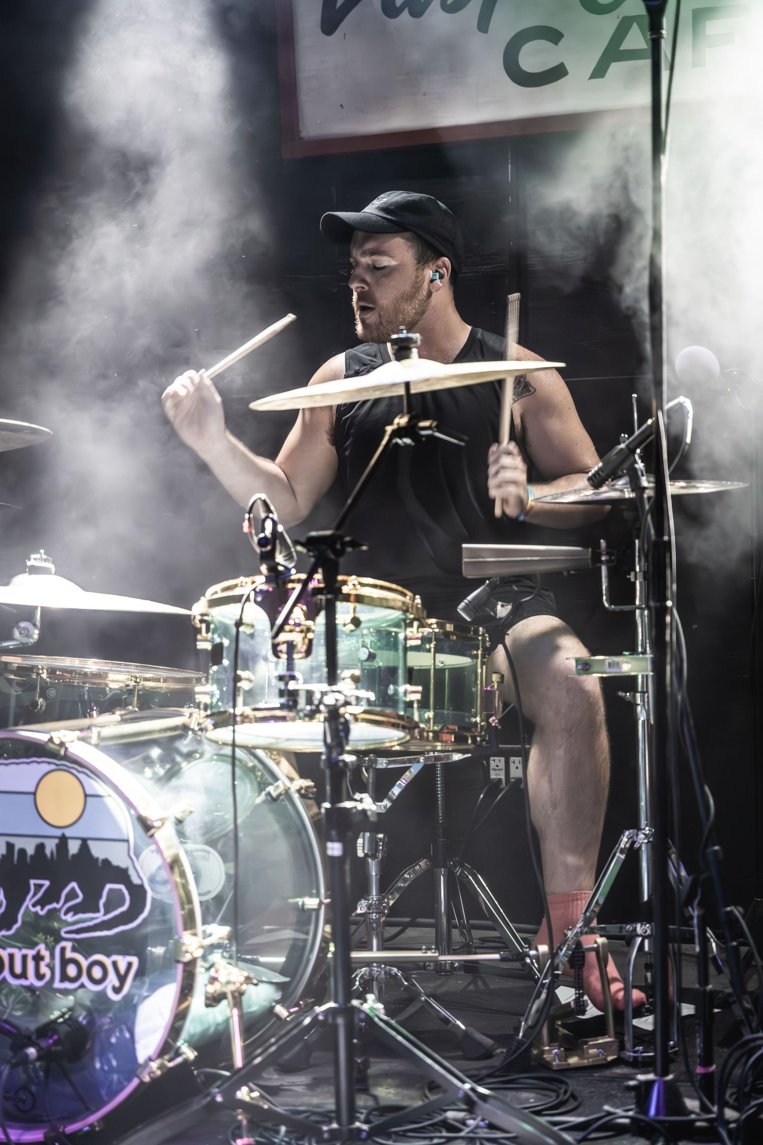 Drummer performs passionately behind a drum kit with smoke effects in atmospheric stage lighting.