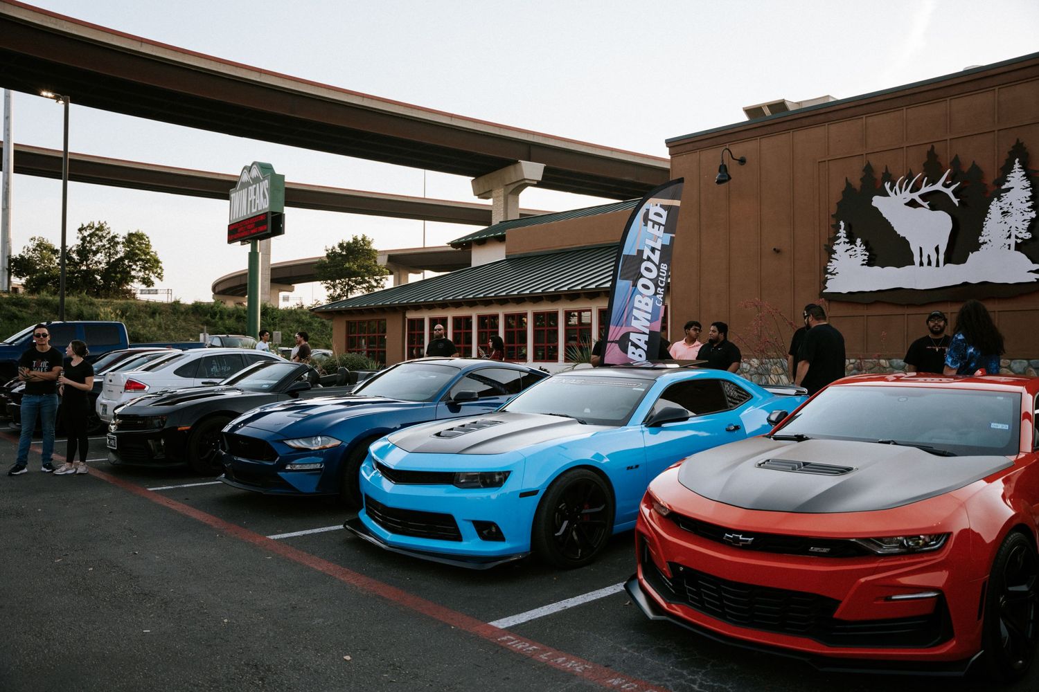 A row of modified Chevrolet Camaros in blue and red displayed at a car meet in a parking lot.