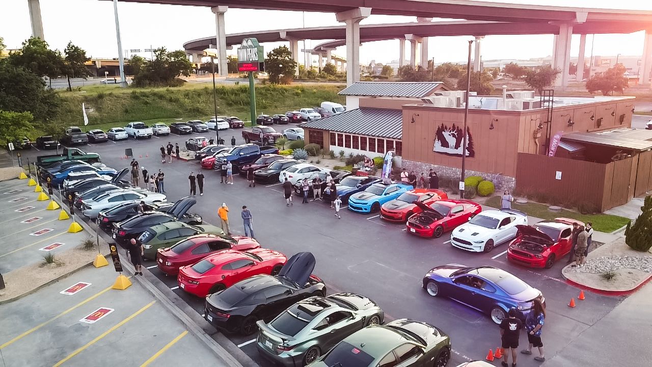 Sunset view of organized car meet showing rows of modified vehicles in restaurant parking lot.