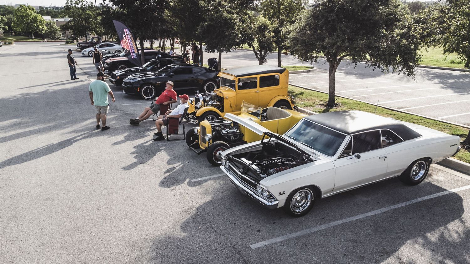 Classic cars lined up at an outdoor auto show including vintage Chevrolets and muscle cars.