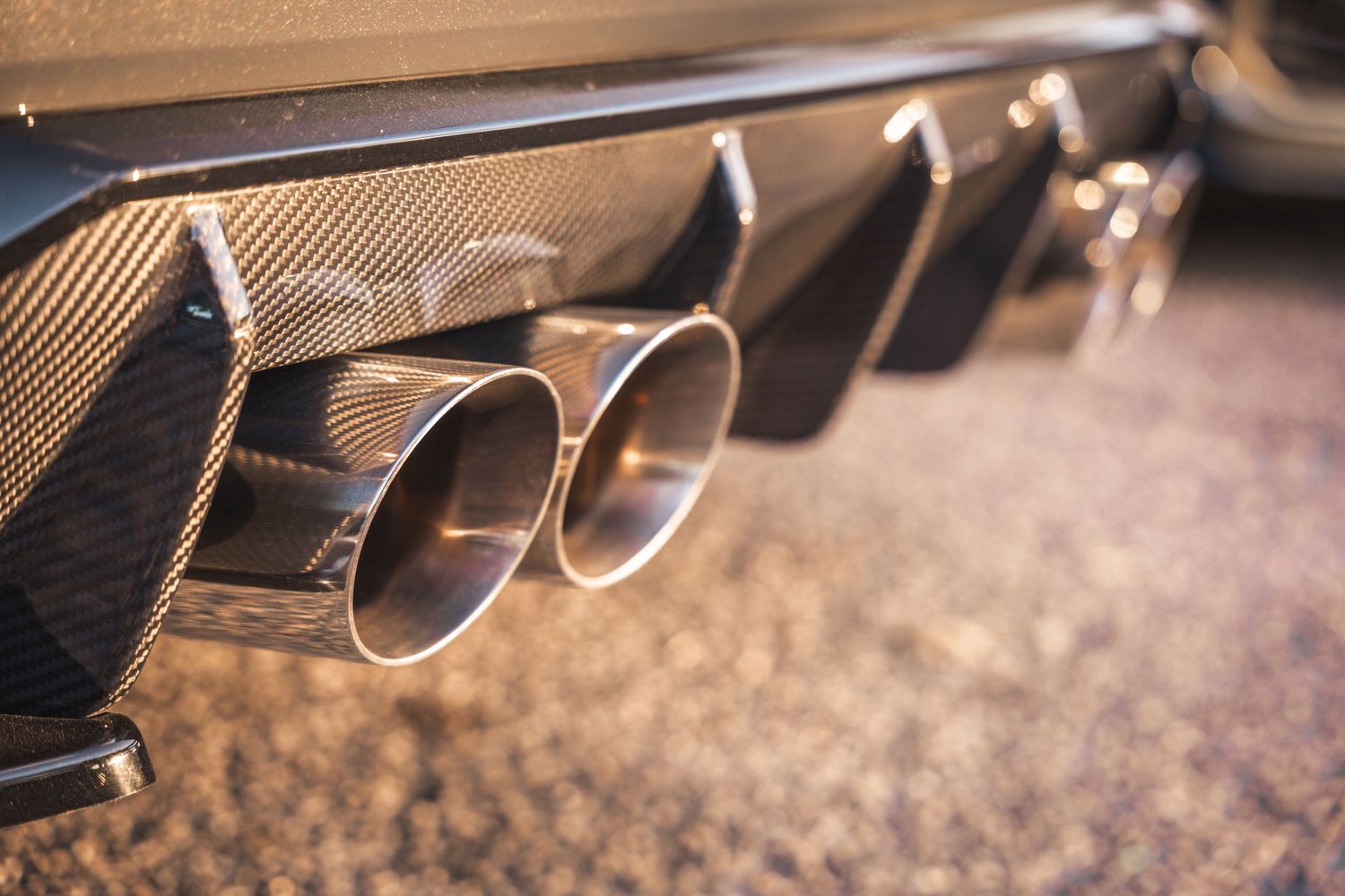 Close-up detail shot of quad exhaust tips on a performance car with carbon fiber diffuser.