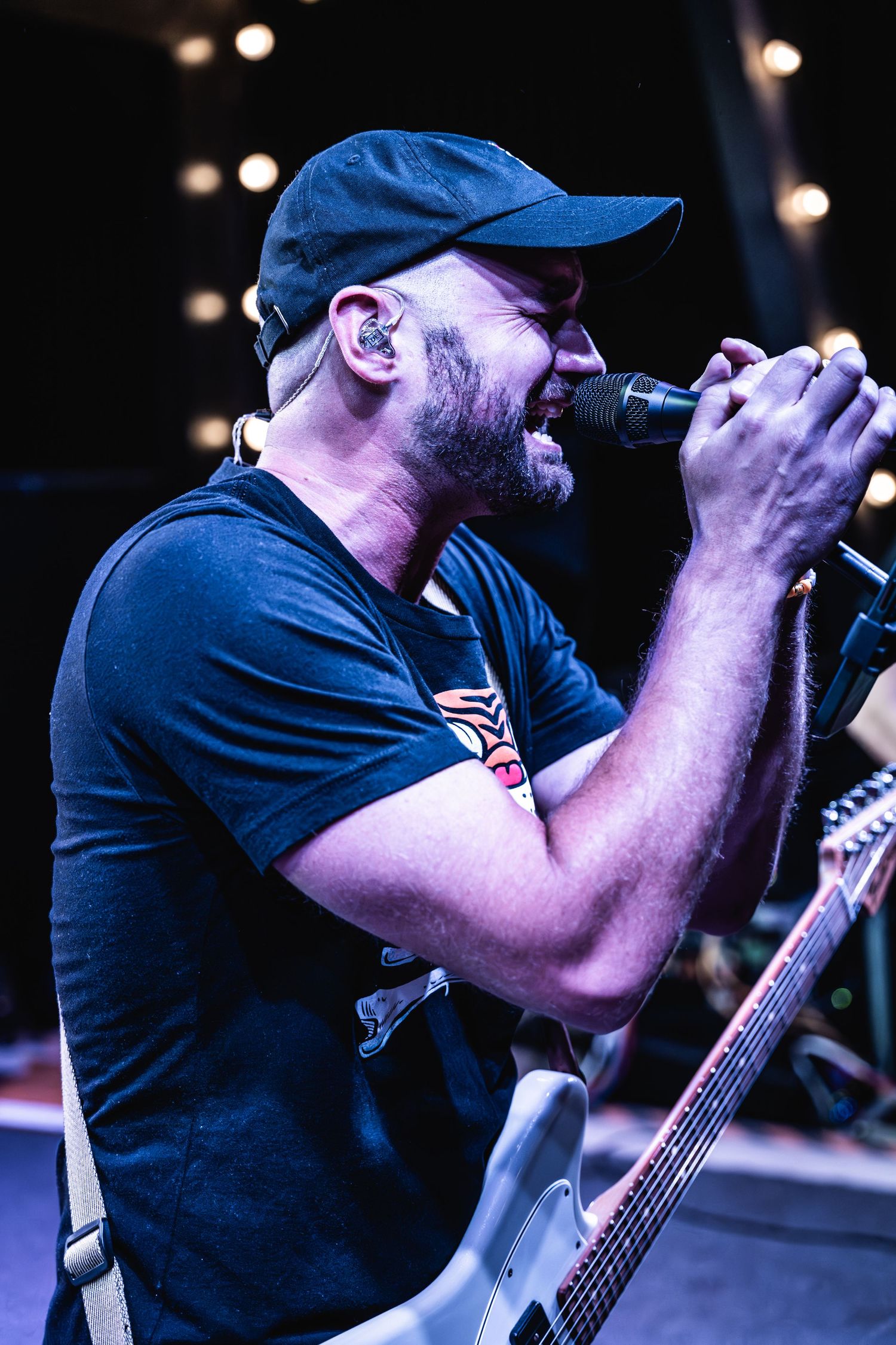 Performer in blue baseball cap singing into microphone during energetic concert performance.