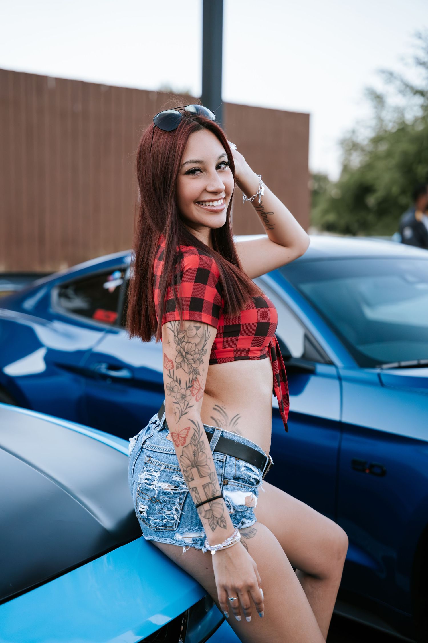 Casual street fashion shoot with plaid crop top against parked cars.