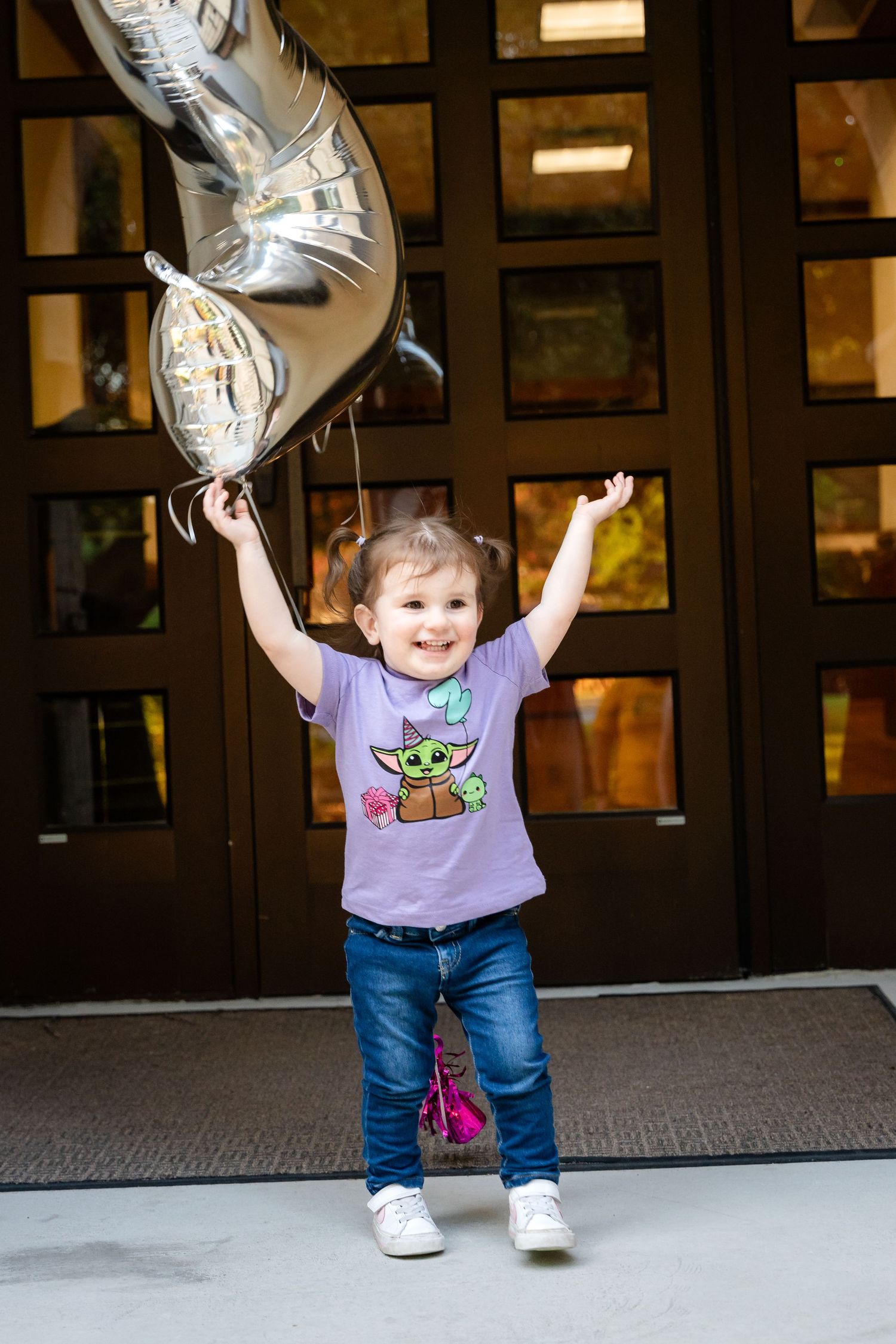 A joyful child in a purple shirt holds silver balloons while celebrating.