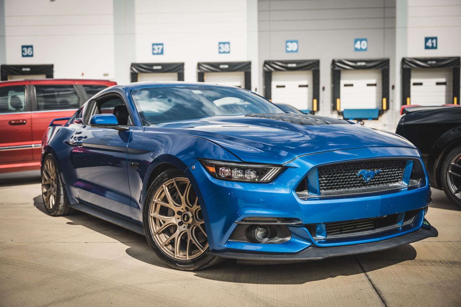 Bright blue Ford Mustang with custom wheels parked in front of loading dock doors.