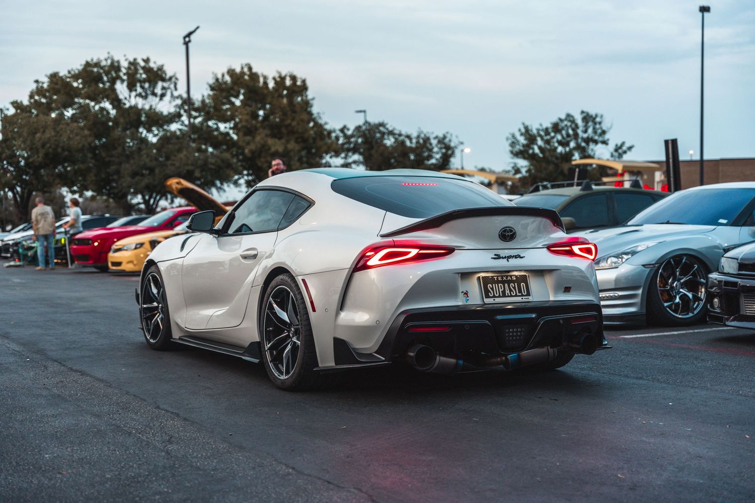 Silver Toyota Supra sports car with aggressive styling parked in a lot at dusk.