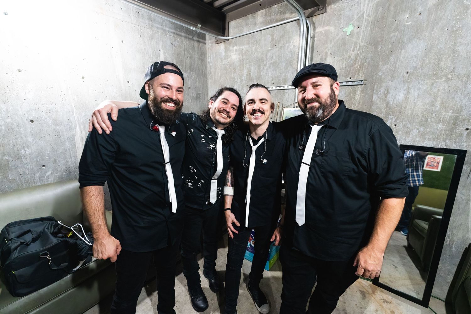 Group wearing matching black outfits and white ties pose together backstage.