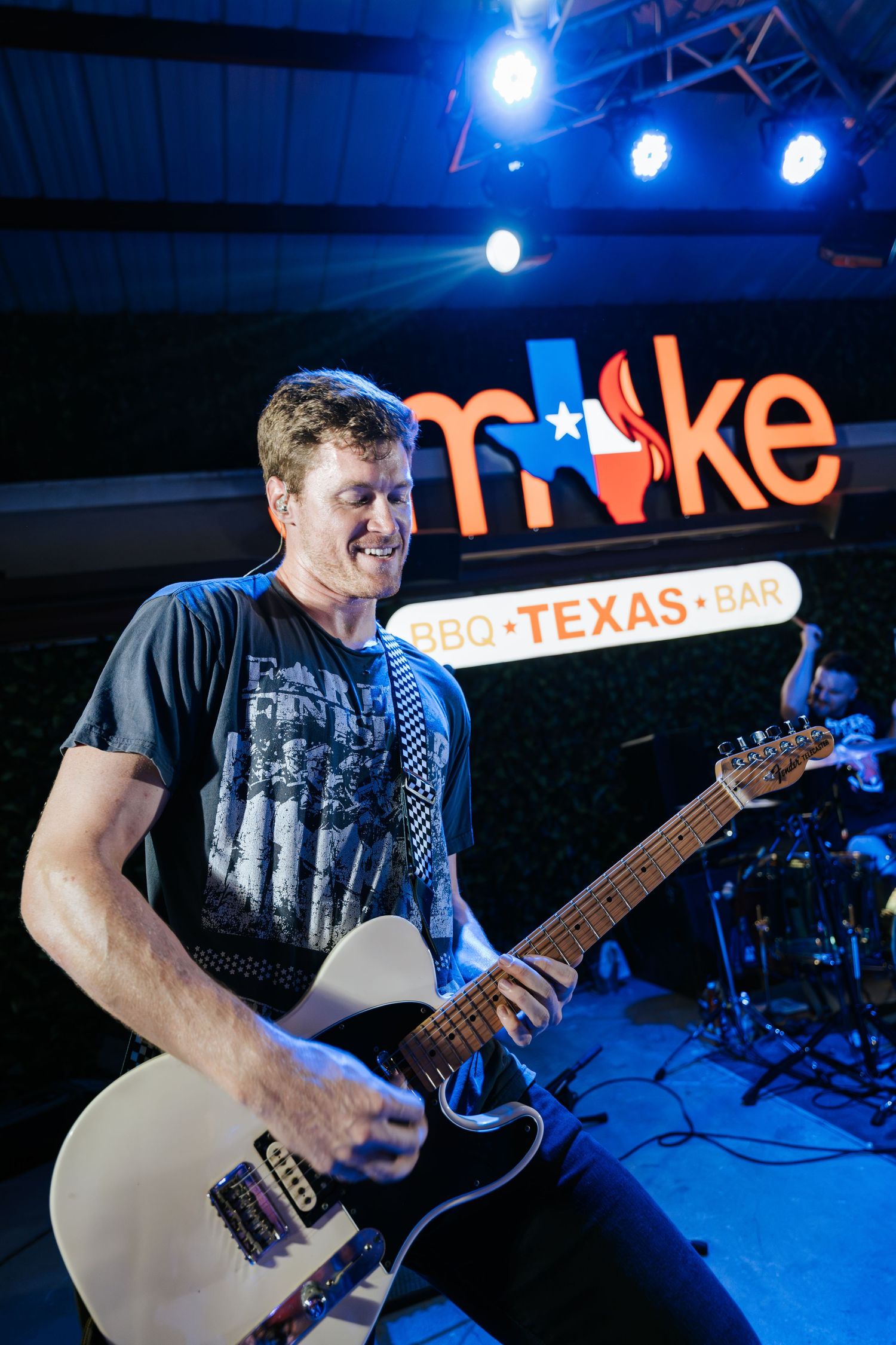Musician playing white electric guitar under blue stage lights with Smoke venue signage.