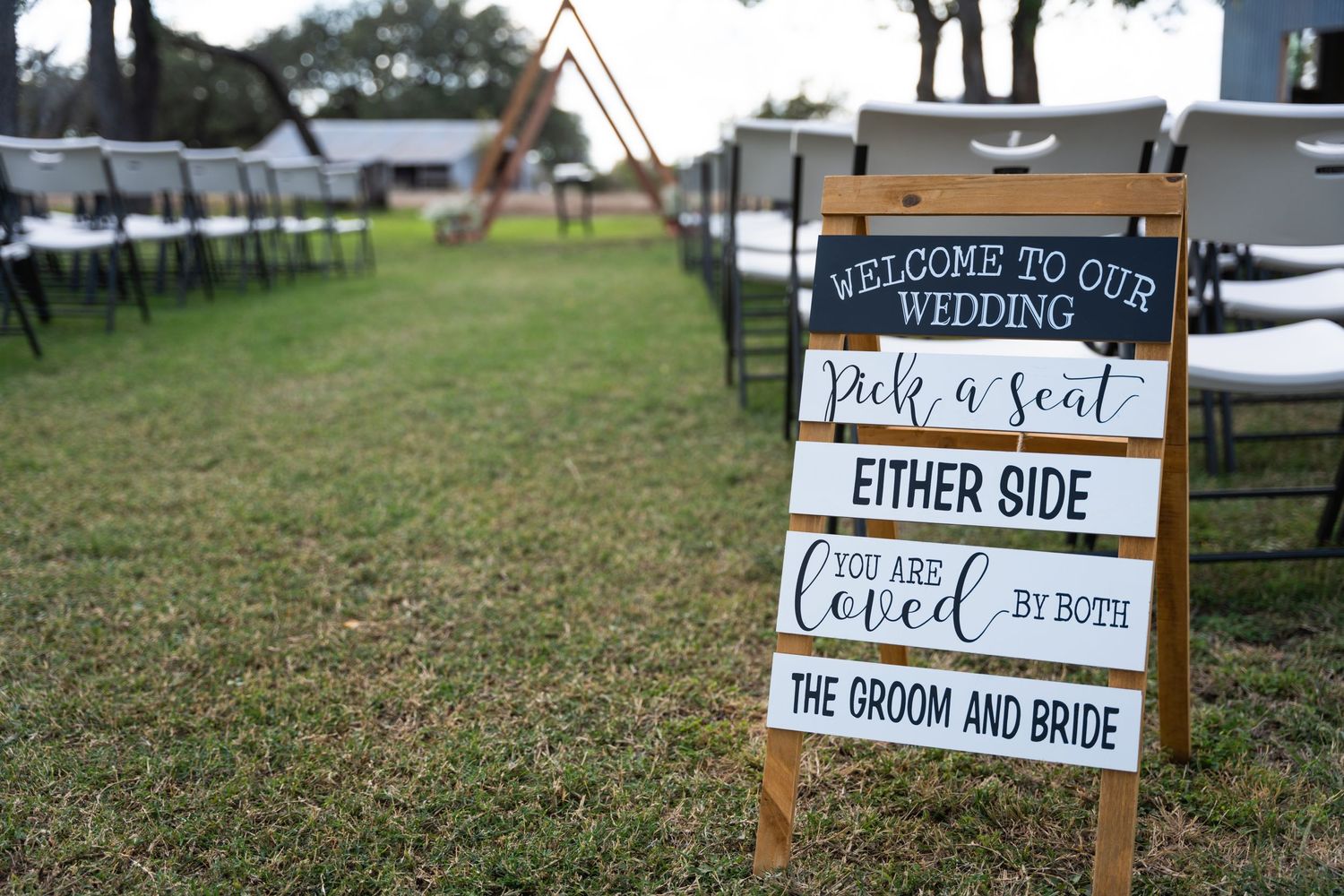 A rustic wedding seating sign displayed on a wooden stand in an outdoor ceremony setting.
