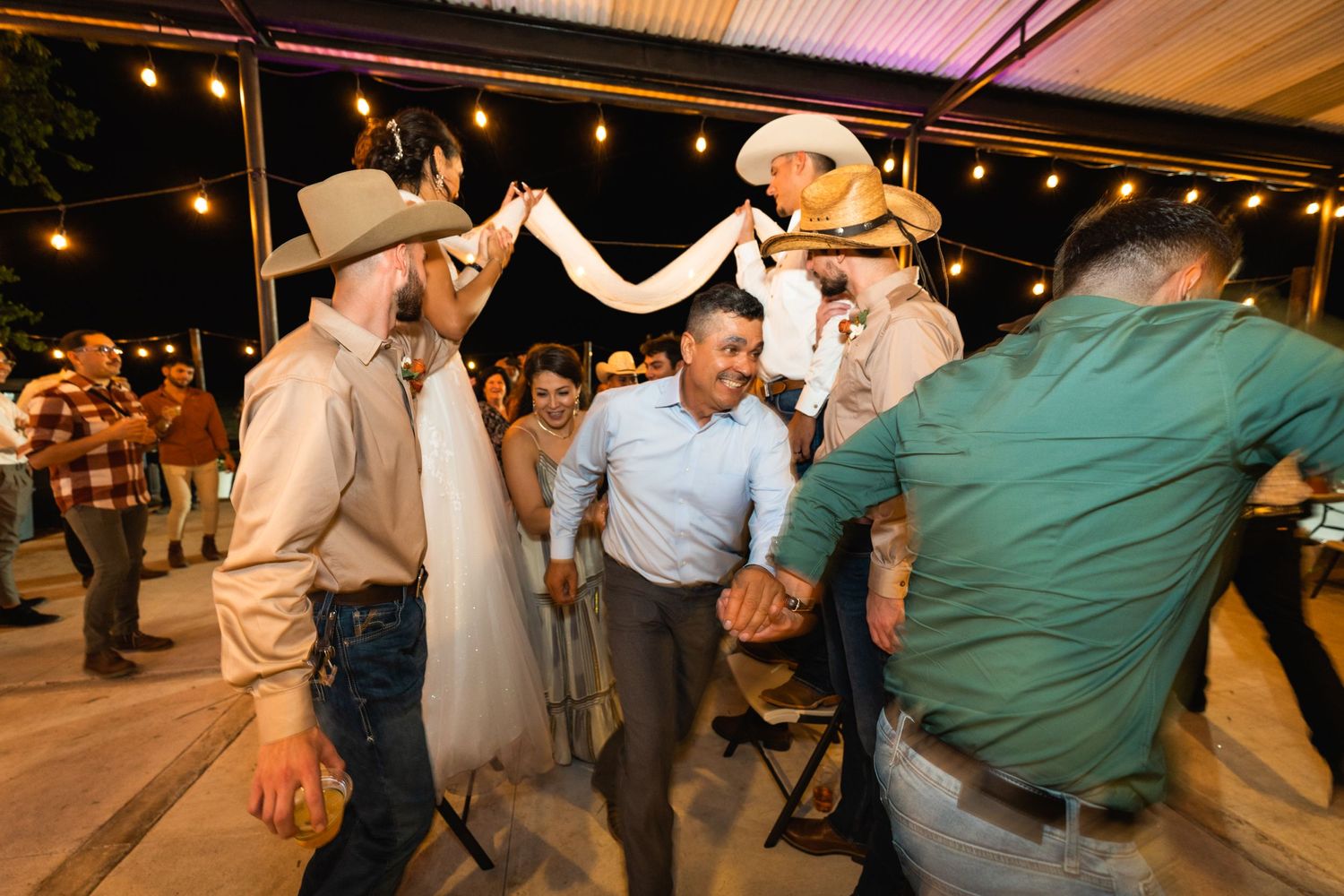 Party guests form an arch tunnel while dancing at a festive country-western themed event.