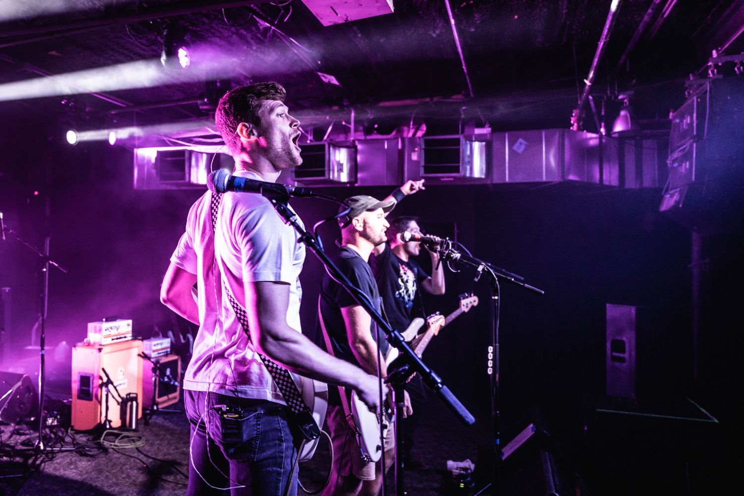 Musicians perform under pink and purple stage lights during live concert.