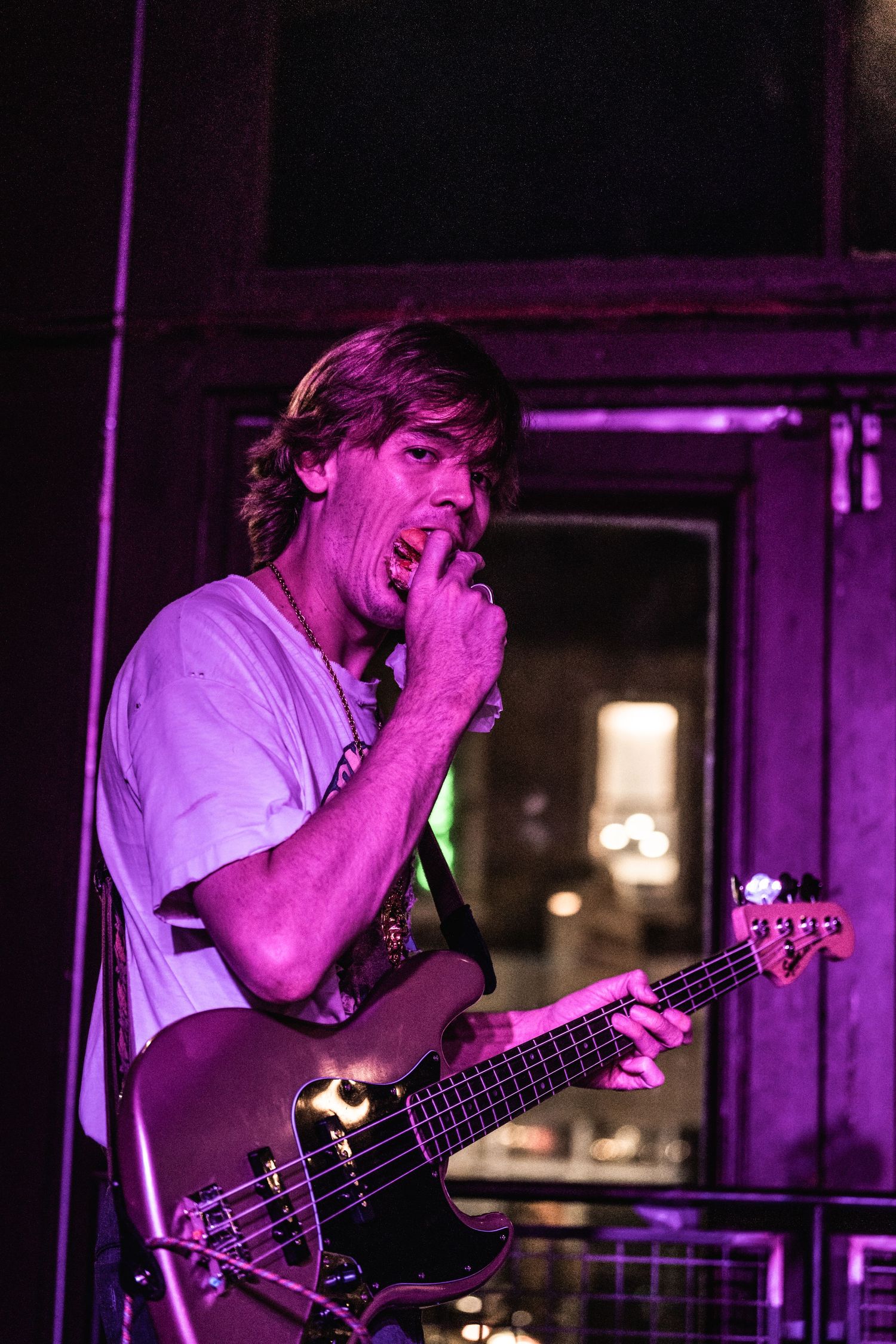 Bass guitarist performing with emotion during a live music show under purple stage lights.
