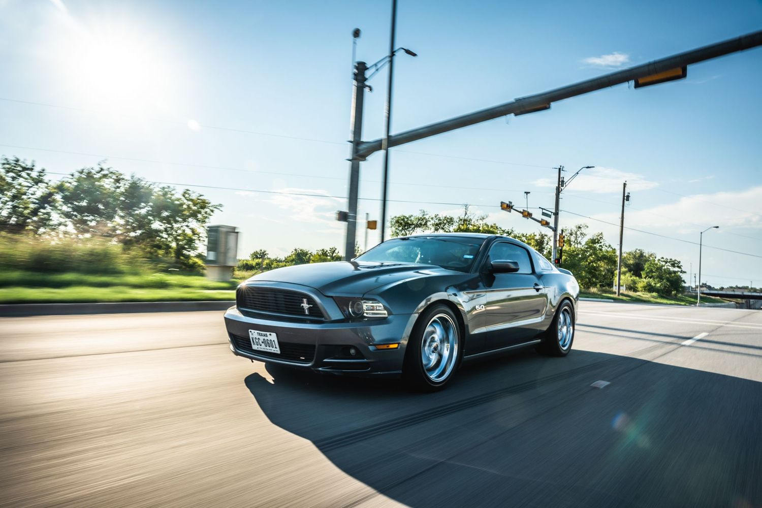 Blue Ford Mustang cruising on urban street with traffic lights overhead.