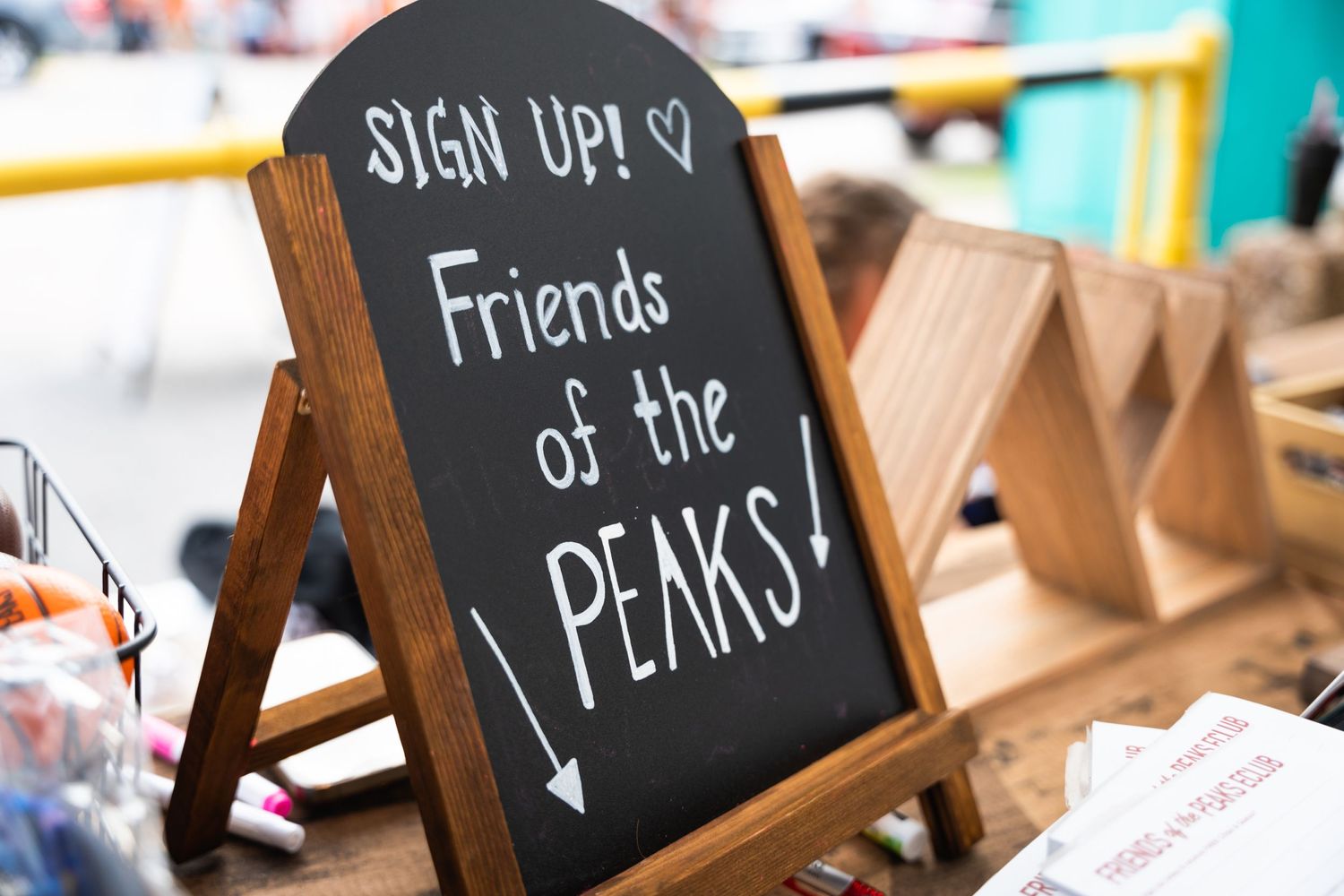 Chalkboard sign reading 'Sign Up! Friends of the PEAKS!' with wooden displays.