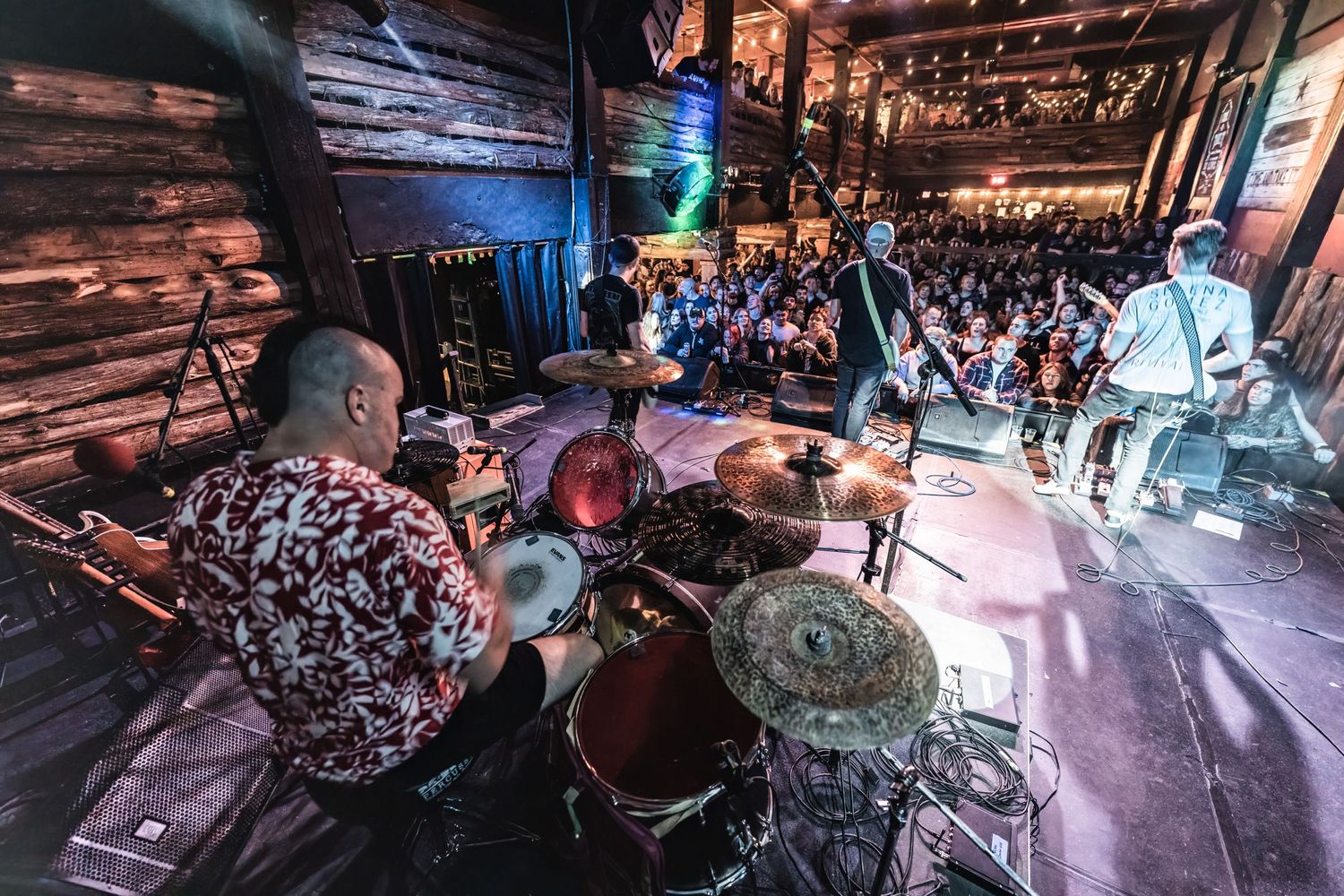 Wide angle shot of band performing on stage with crowd visible in foreground.