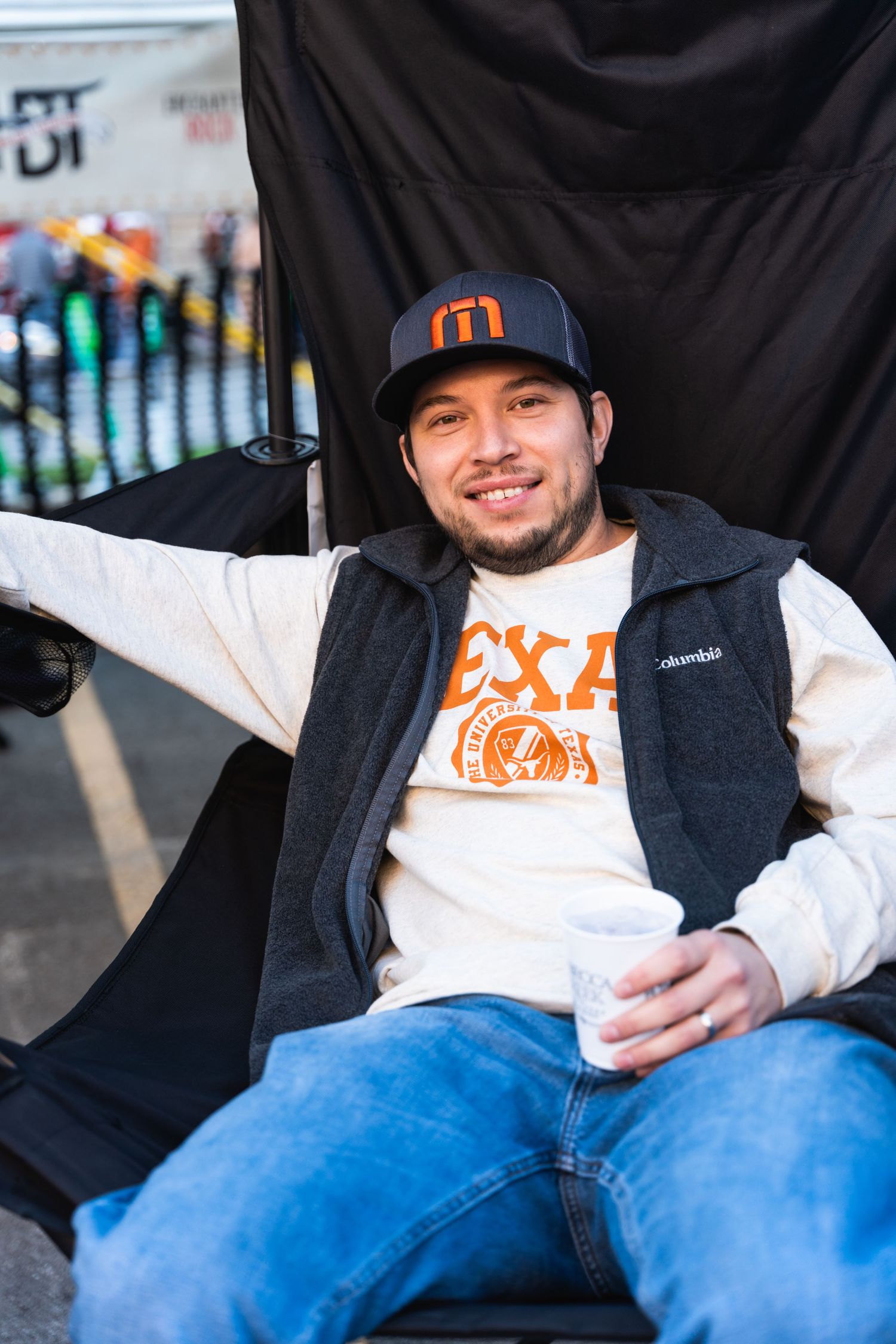 A person wearing a navy baseball cap and vest relaxes at an outdoor event.