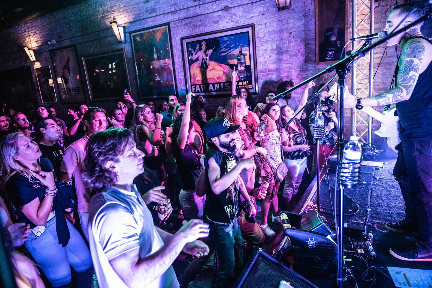 Enthusiastic concert crowd dancing under purple stage lights in a packed venue.