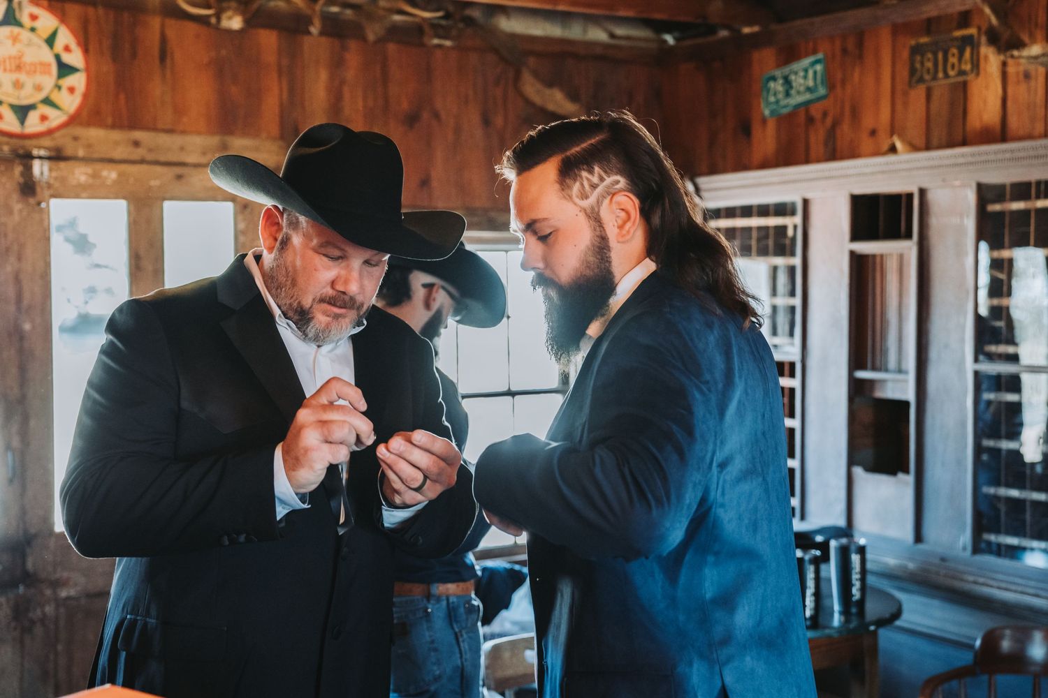 Two men in cowboy hats examine something together in a rustic wooden interior.